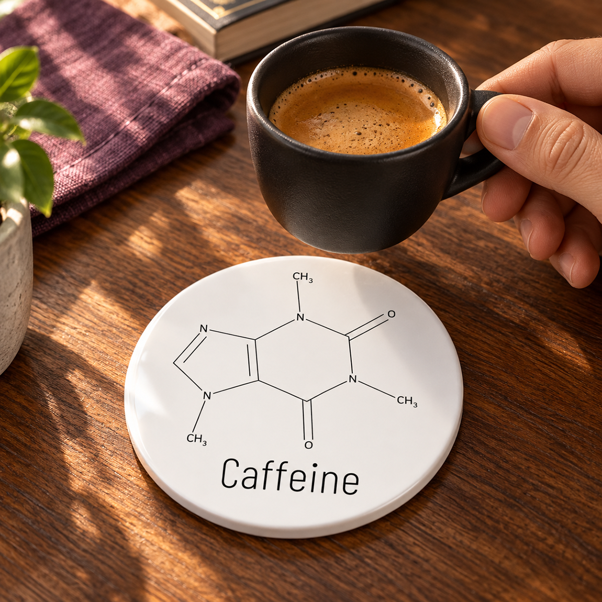 Caffeine molecule ceramic coaster on a walnut table as a black espresso cup is lifted, with warm sunlight and plum linen.