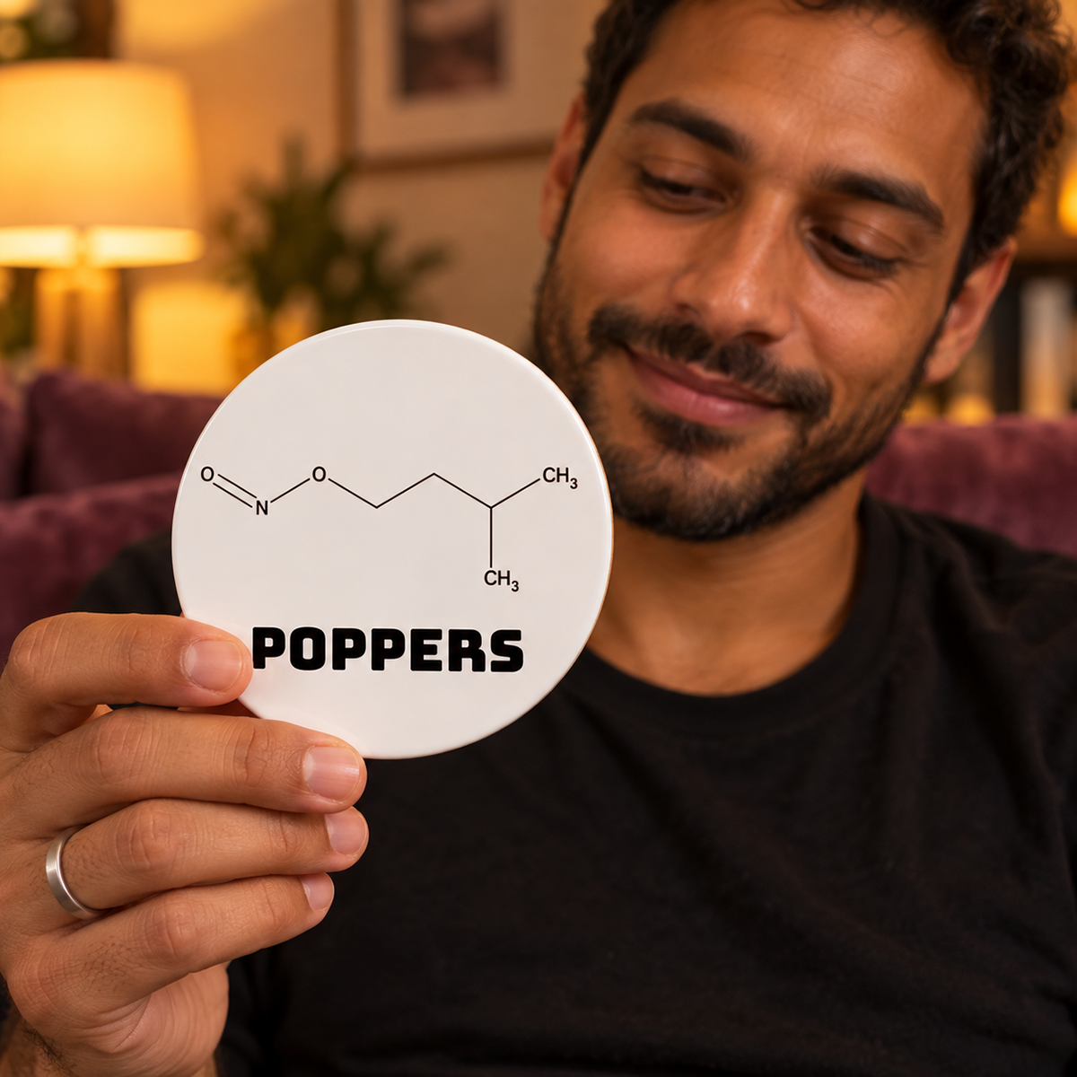 A man holds a round white Poppers molecule ceramic coaster, showing the Street Names design in a warm apartment setting.